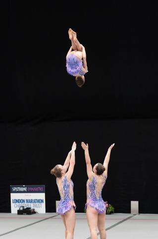 Gymnast performing a tuck back from 2 bases in a trio